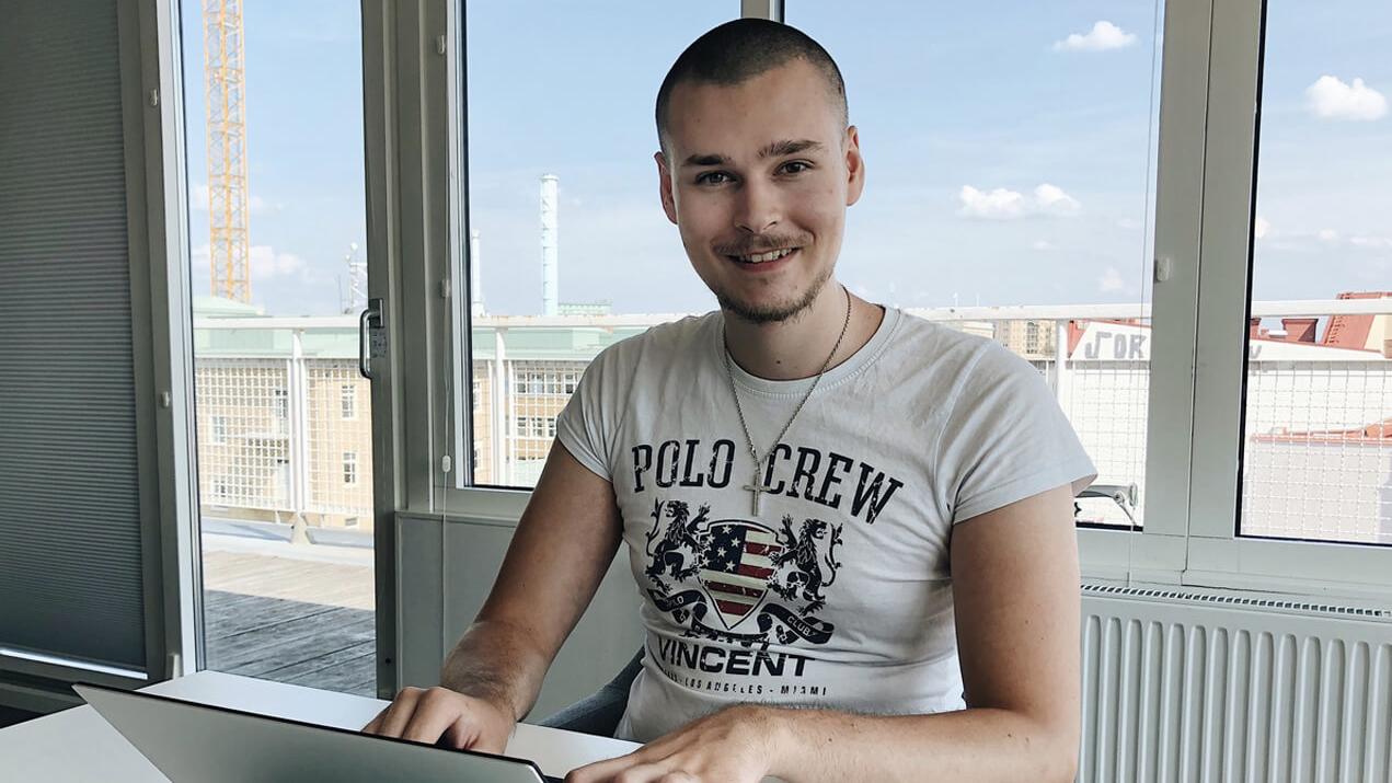 Leende man i vit t-shirt vid en laptop på ett ljust kontor