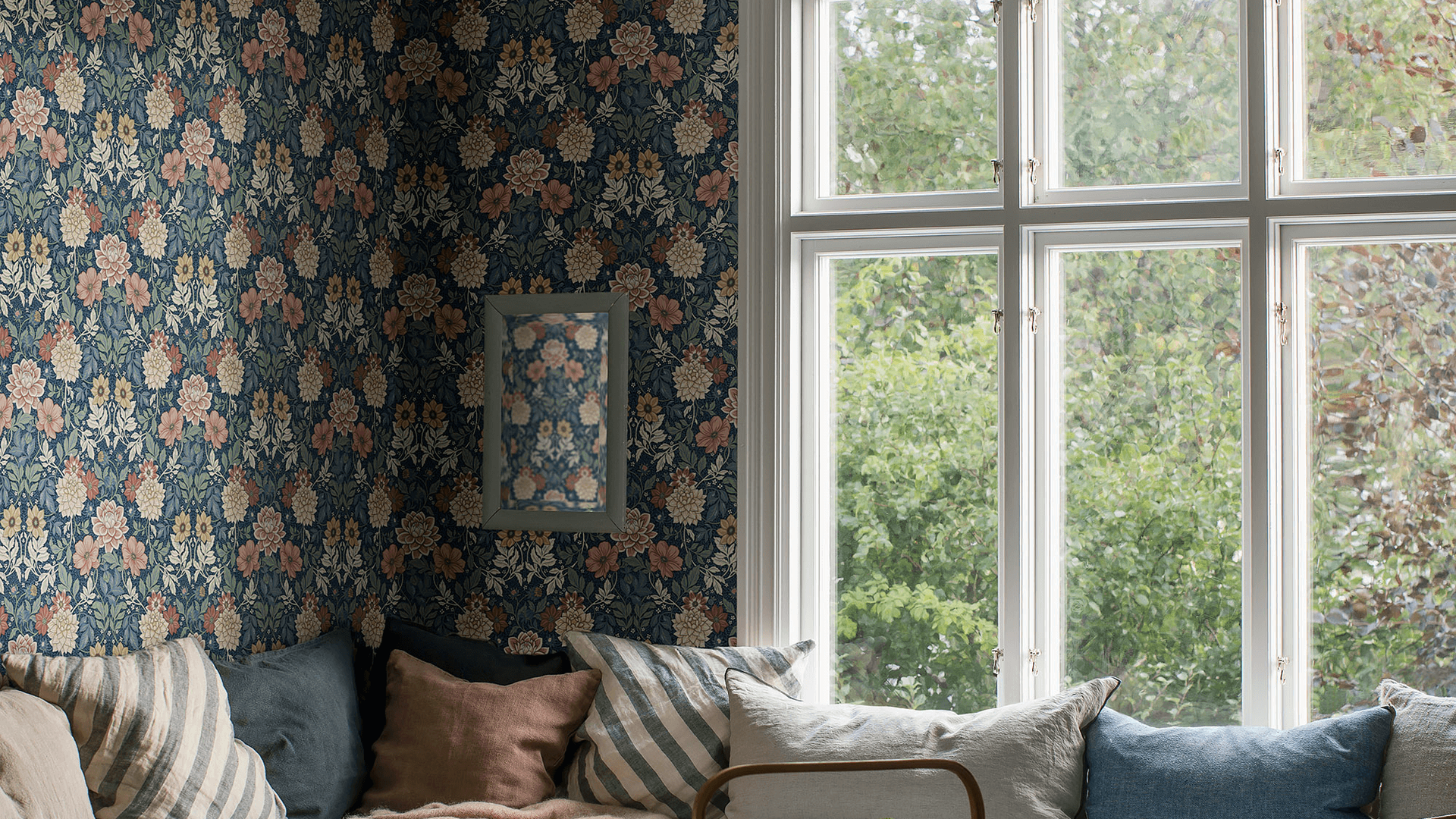 Soffhörna med blommig mörkblå tapet, kuddar och ett stort spröjsat fönster