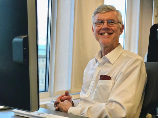 Leende man i vit skjorta som sitter vid en datorskärm på ett kontor