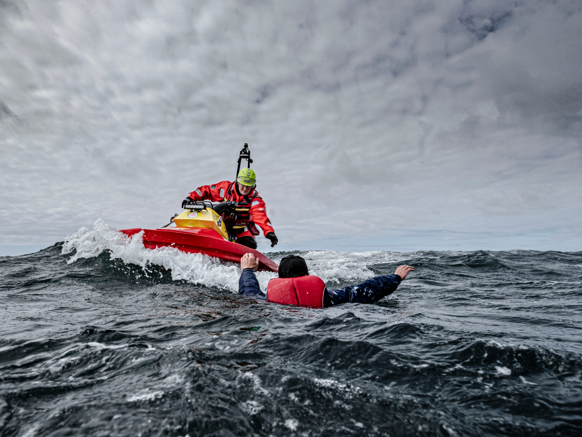 Sjöräddare på en vattenskoter når fram till en person i flytväst i det kalla havet