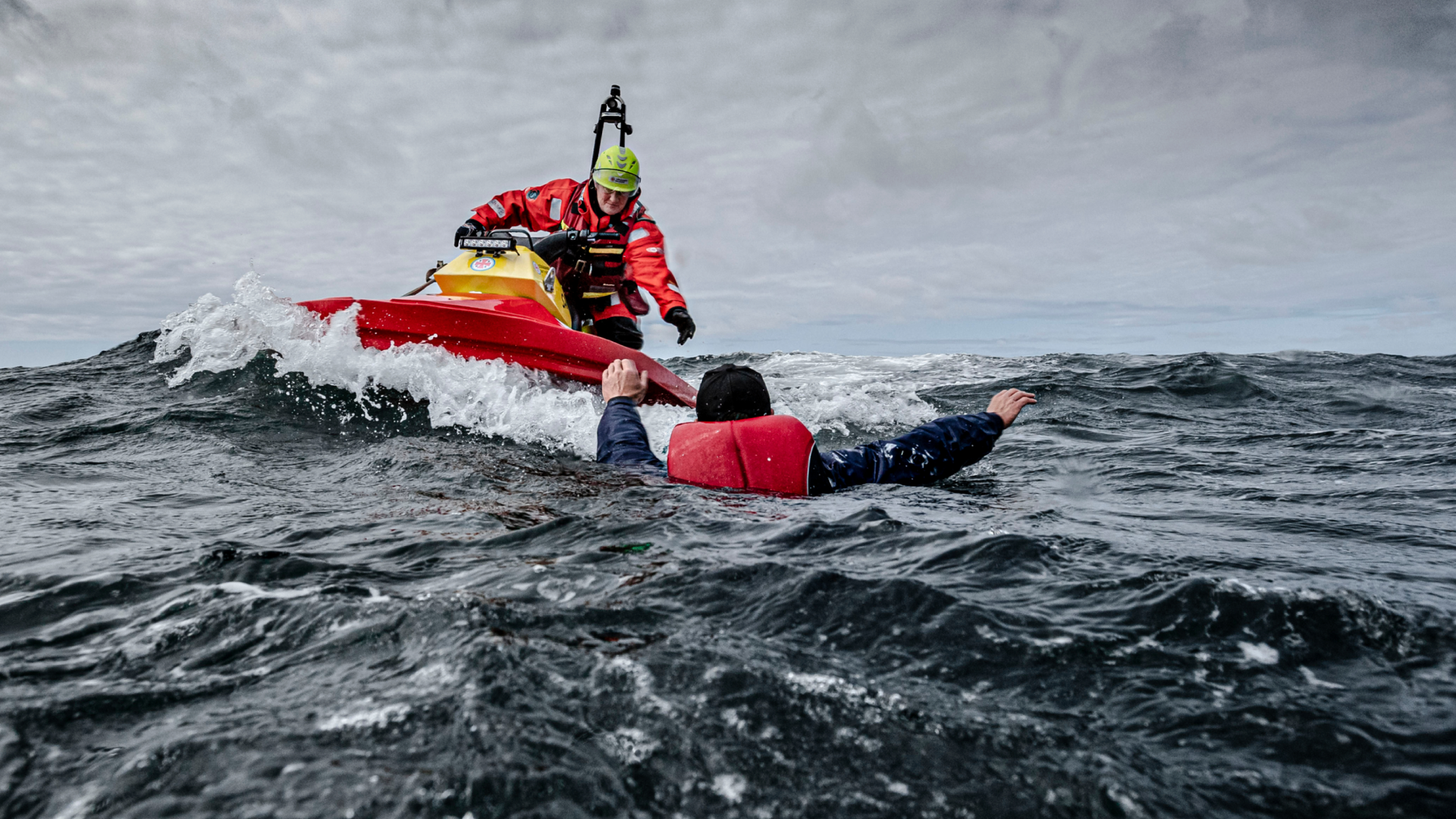 Sjöräddare på en vattenskoter når fram till en person i flytväst i det kalla havet