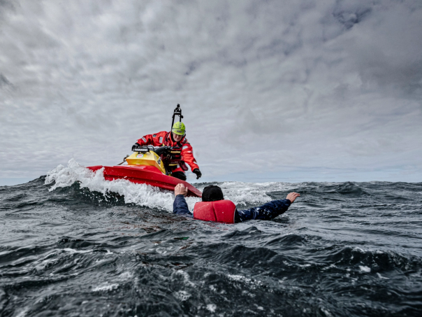 Sjöräddare på en vattenskoter når fram till en person i flytväst i det kalla havet