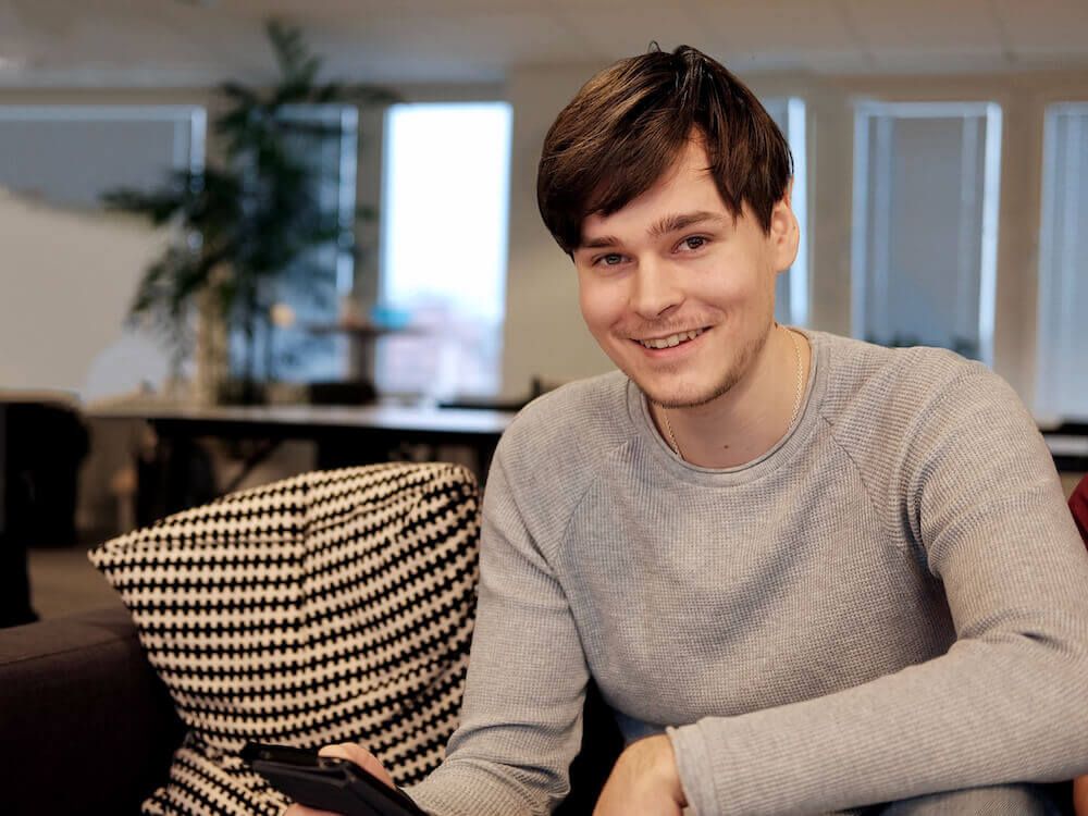 Leende ung man i grå tröja som sitter i en soffa på ett kontor