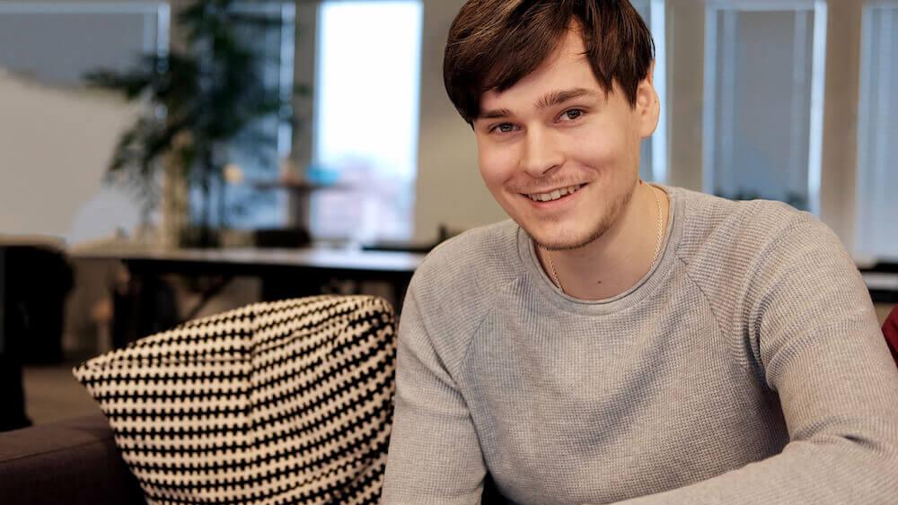 Leende ung man i grå tröja som sitter i en soffa på ett kontor