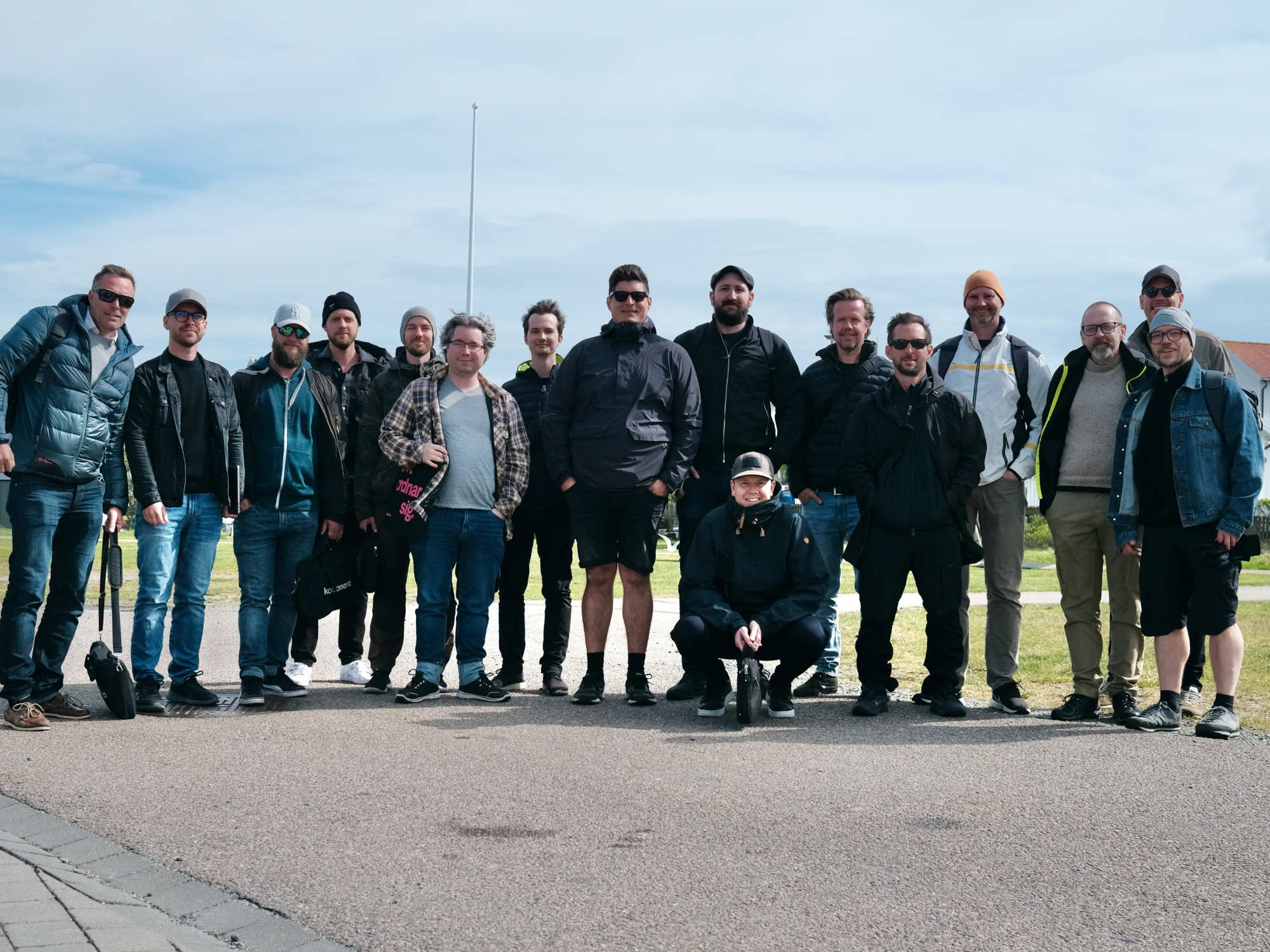 Gruppfoto med ett femtontal personer utomhus på en gångväg en molnig dag