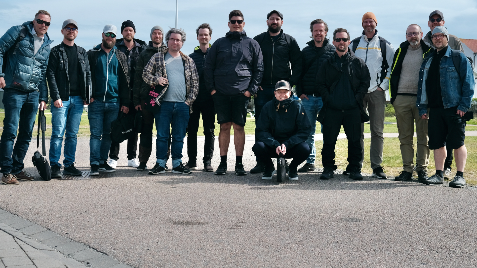 Gruppfoto med ett femtontal personer utomhus på en gångväg en molnig dag