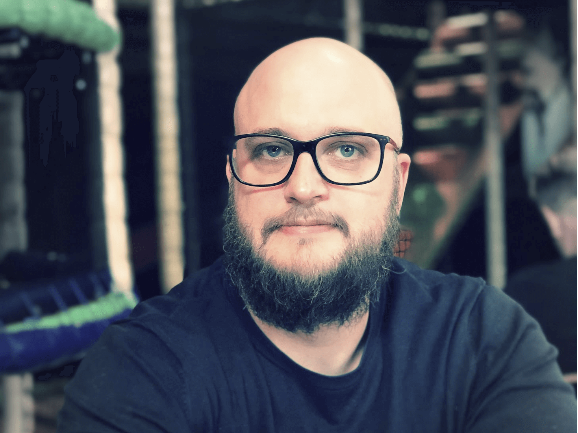 Porträtt av en man med skägg och glasögon i mörk t-shirt
