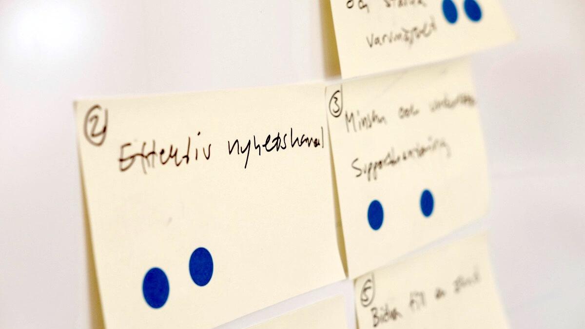 Handskrivna lappar på en whiteboard med blå röstprickar, bland annat ”Effektiv nyhetskanal”