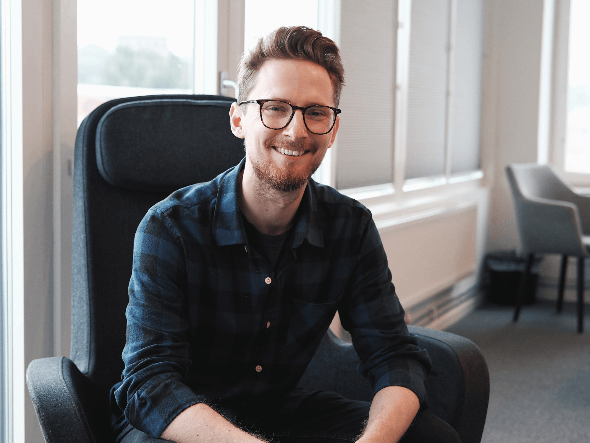 Leende man med glasögon och rutig skjorta som sitter i en kontorsstol