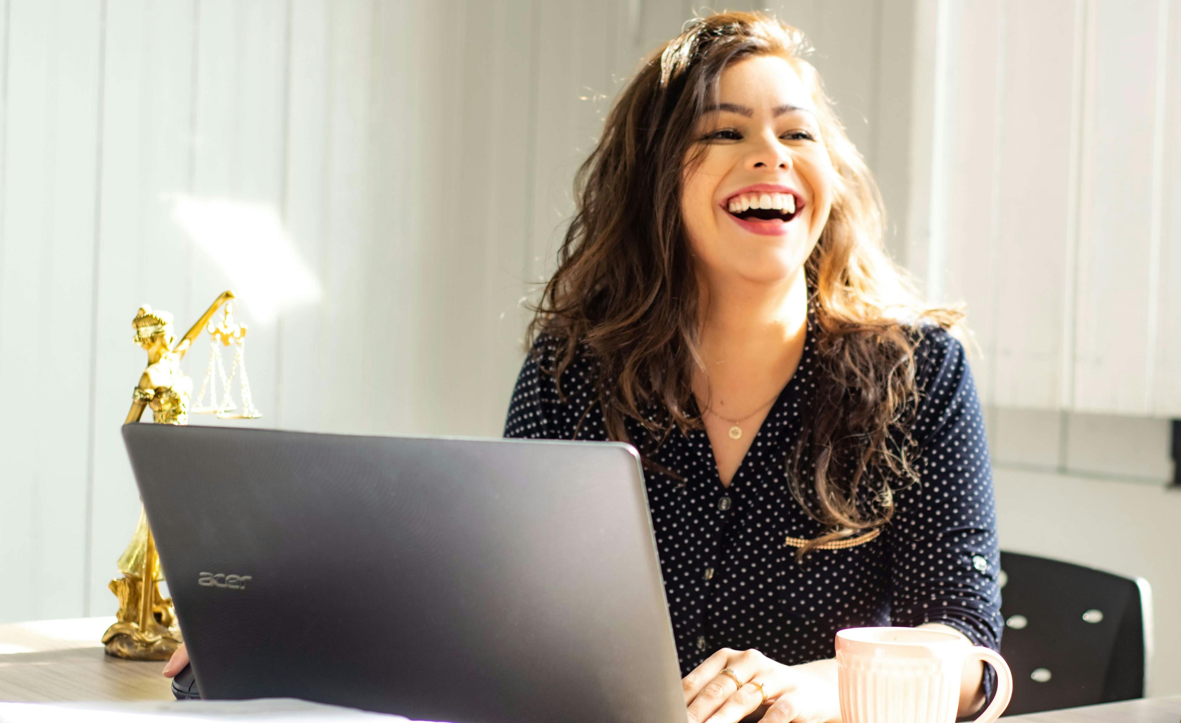 En glad tjej som ler, framför sin laptop