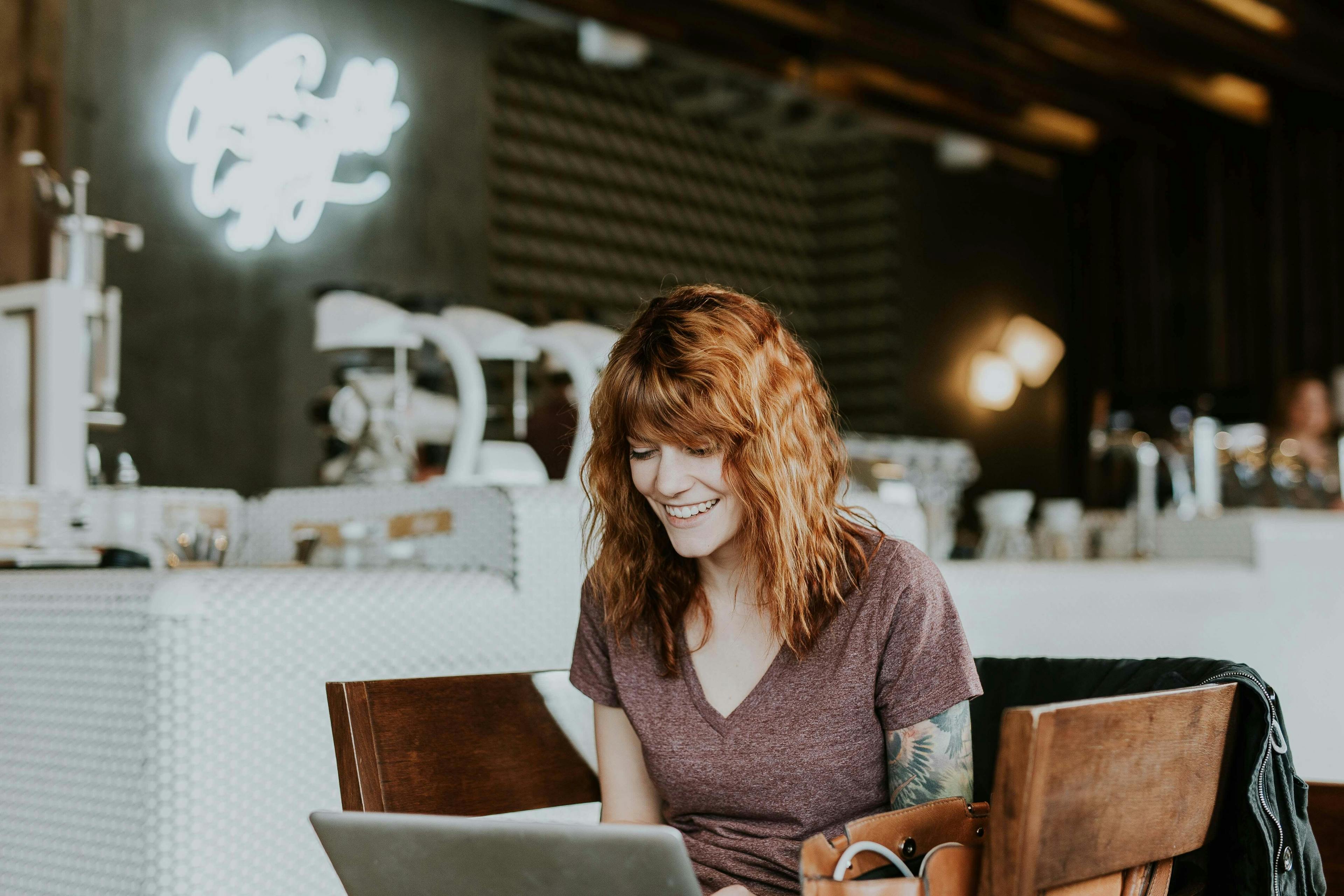 Bild med en kvinna som sitter framför sin laptop, synligen glad