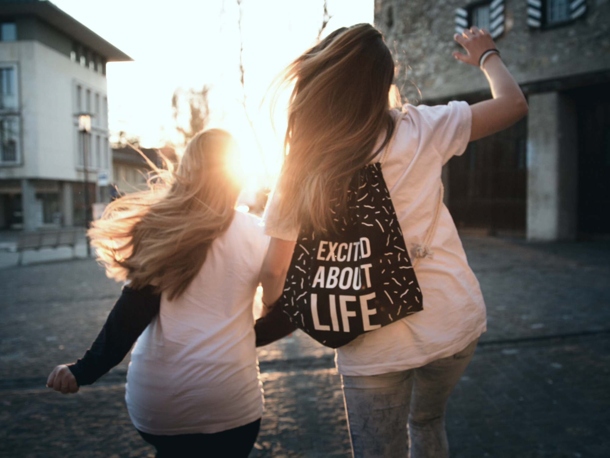 Två barn som springer i motljus. En av dem har en ryggsäck med texten "Excited about life"