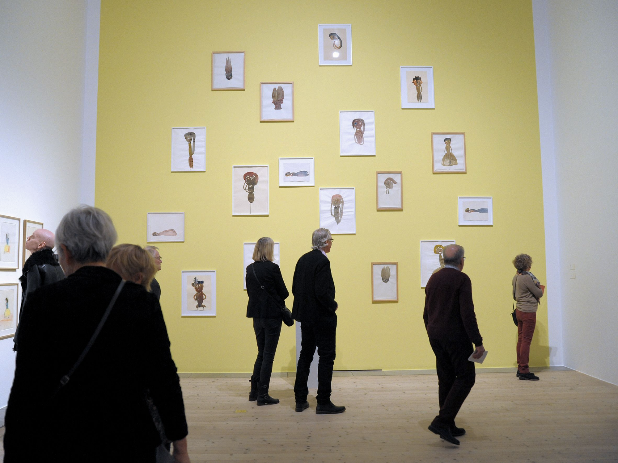 Ett gult rum med akvarellmålningarna på väggarna med besökare som tittar på dem