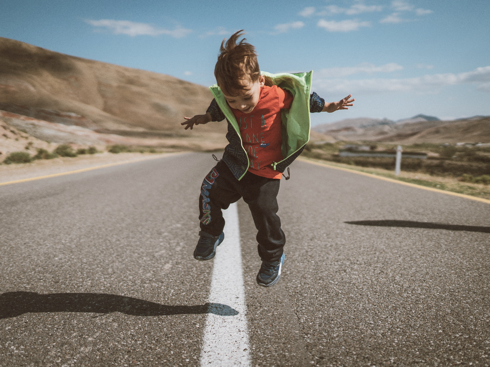 Foto av en ung pojke som gör ett hopp på mittlinjen på en vägsträcka, berg i bakgrunden